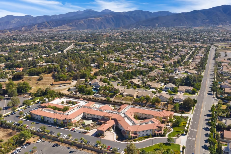 Aerial view of Estancia Del Sol senior living facility surrounded by residential neighborhoods with mountains in the background under a clear blue sky.