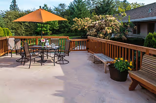 Outdoor wooden deck with table, chairs, orange umbrella, benches, and potted flowers.
