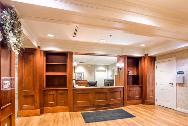 Warmly lit reception desk and lobby area with wooden built-in shelving and a welcome mat.
