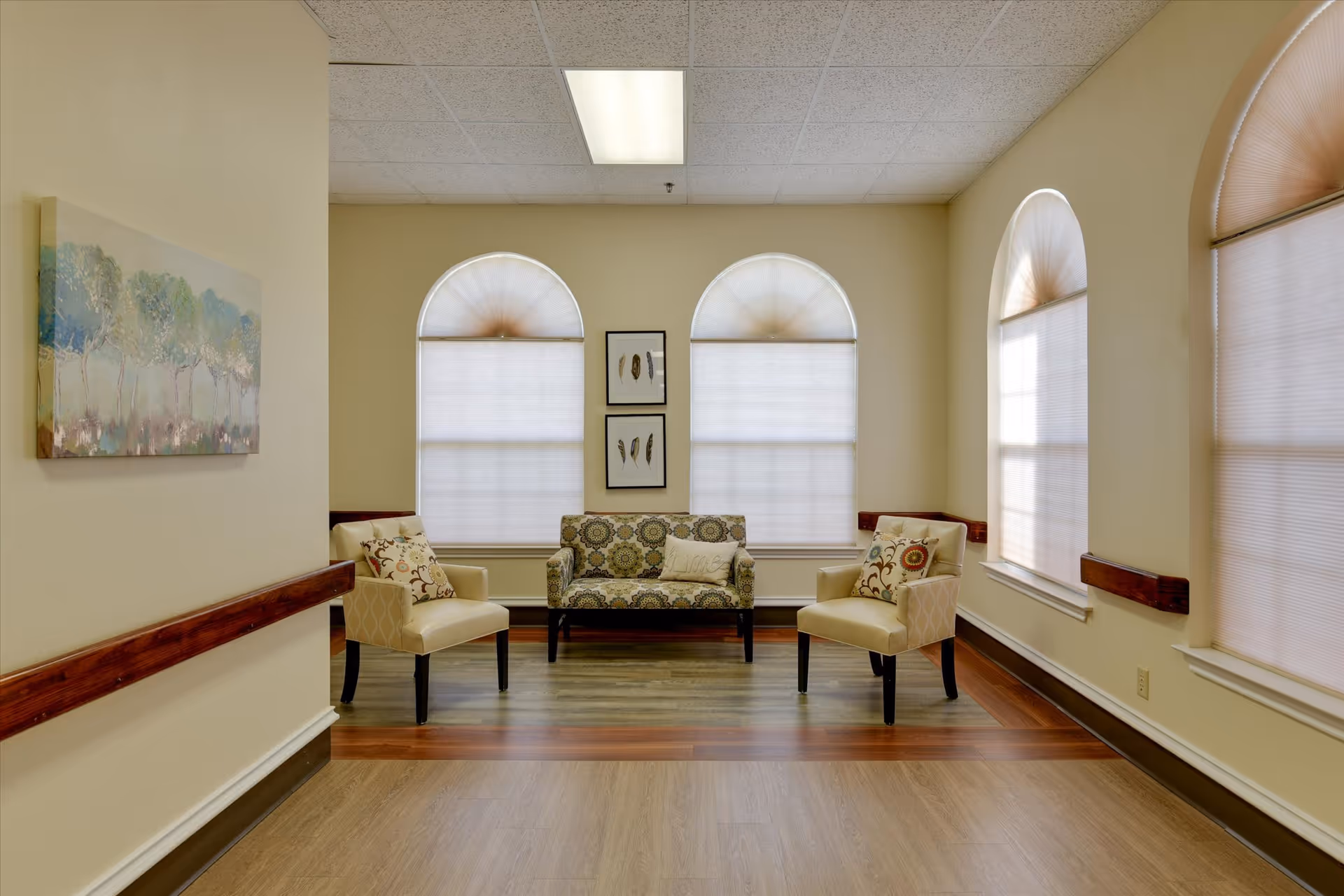 Well-lit sitting area with three arched windows, a patterned loveseat centered between two armchairs and decorative artwork.