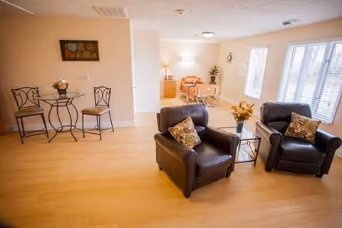 Cozy senior living common area with two leather chairs, a small table, and large windows.