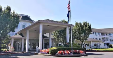 Senior living facility entrance with a covered drop-off area, flagpole, and landscaped garden.