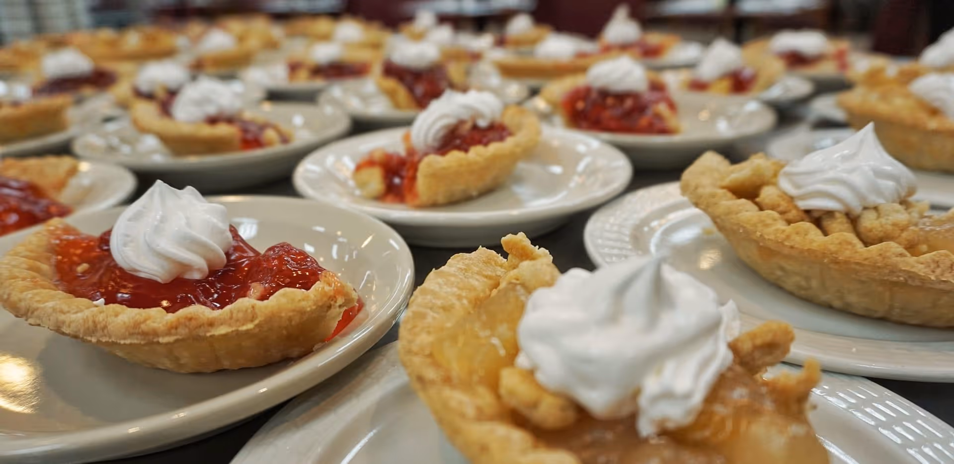 Close-up view of multiple small fruit pies topped with whipped cream, arranged on white plates on a table.