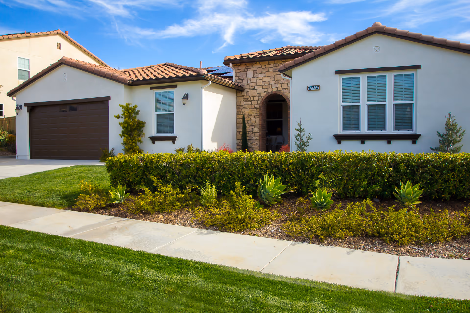 Front exterior of a single-story Mediterranean-style house with a two-car garage, stone entryway, and landscaped lawn.