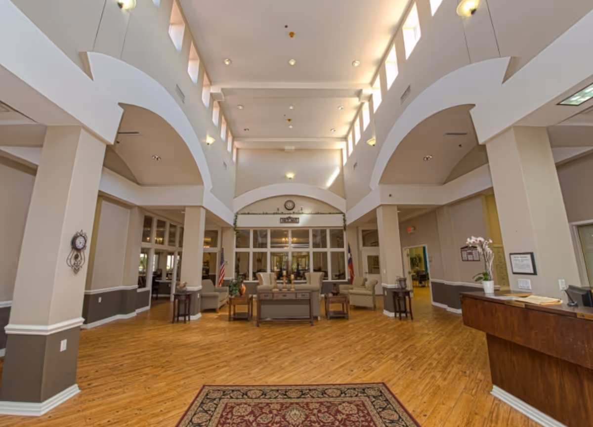 Spacious high-ceilinged senior living lobby with seating areas, a reception desk, and hardwood floors.