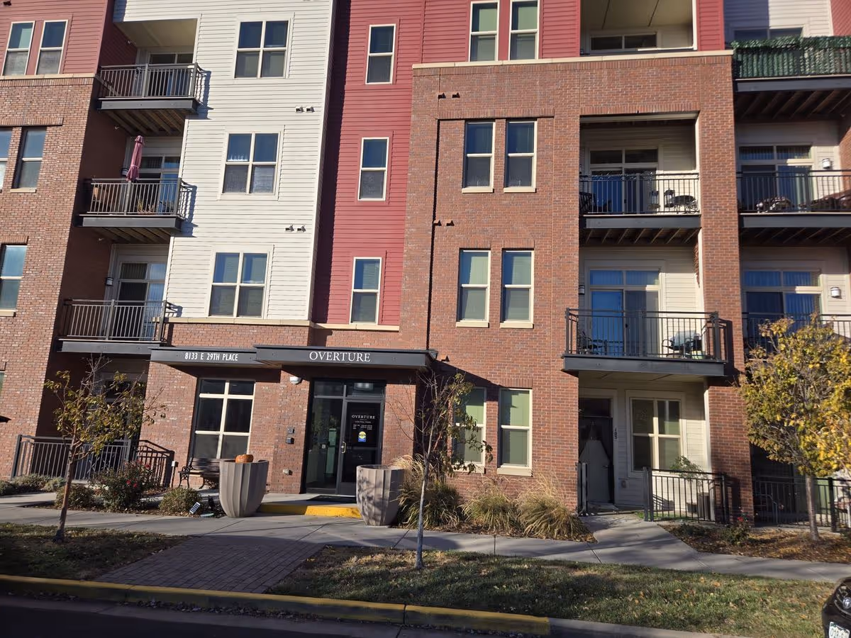 The front entrance of a multi-story brick and siding apartment building with balconies and an 'Overture' awning.