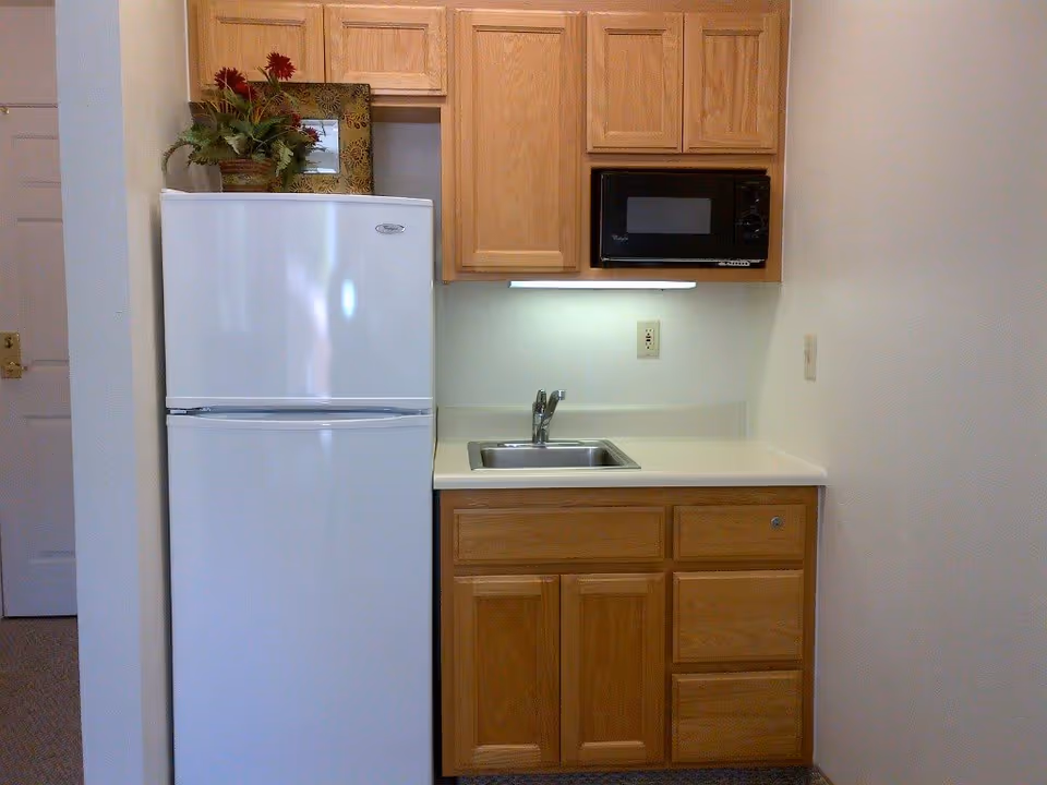 Small kitchenette with a white refrigerator, wooden cabinets, a sink, and a microwave.