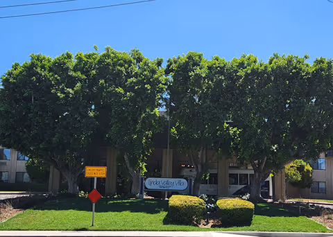 Exterior view of Linda Valley Villa with a sign in front and large trees along the entrance