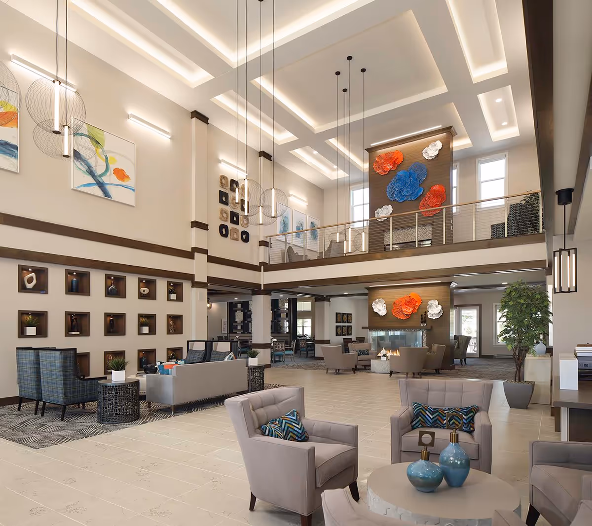 Spacious two-story senior living lobby with modern seating areas, high coffered ceilings, hanging light fixtures, and decorative wall art.