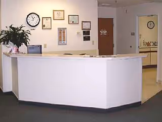 Reception desk in a hallway with framed certificates and a plant.