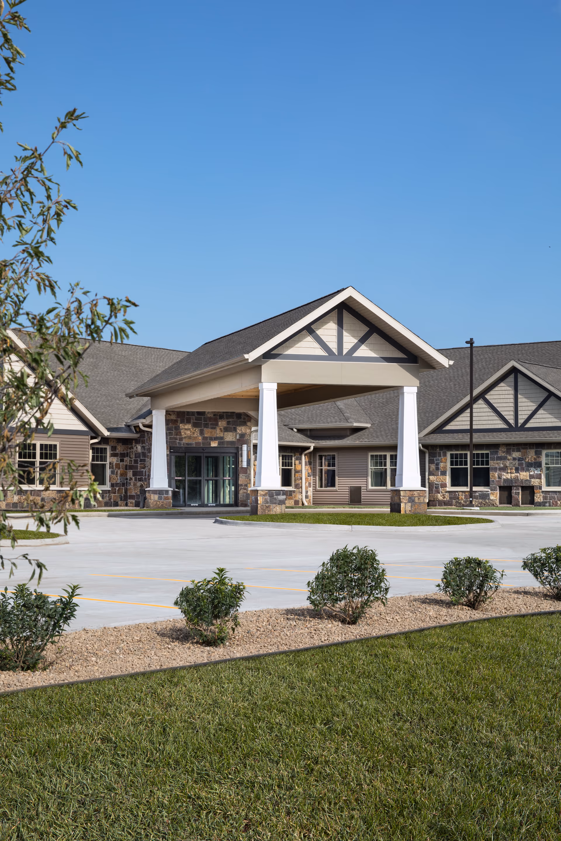 The exterior entrance of The Gardens of Cedar Rapids featuring a covered area and landscaped surroundings.