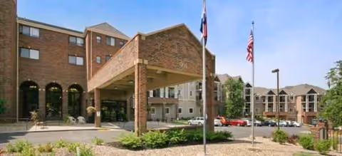Brick senior living facility entrance with a covered drop-off and flagpoles.