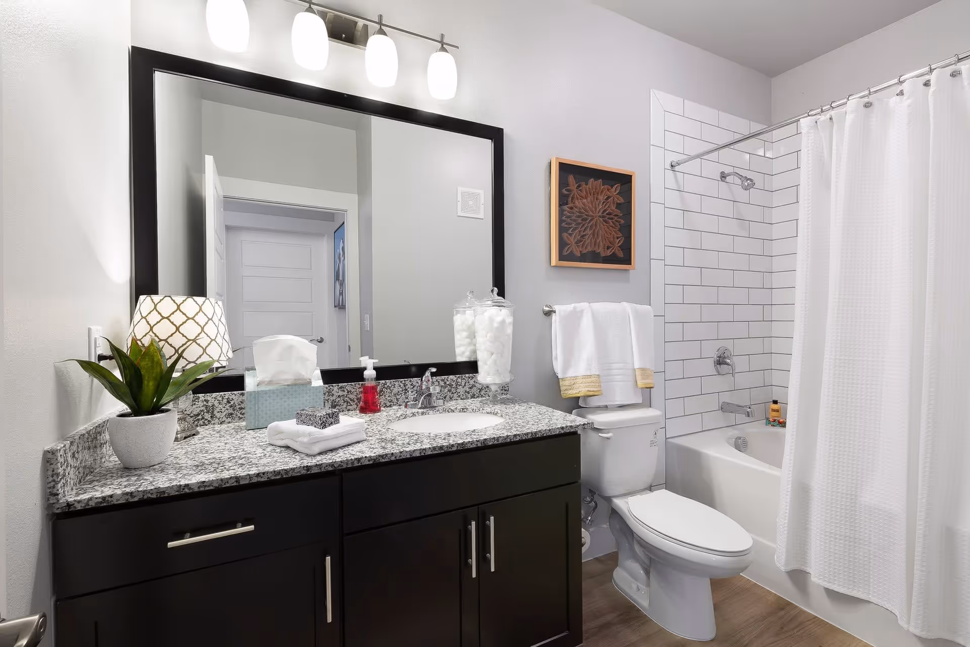 Modern bathroom with a dark vanity and granite countertop, large mirror, toilet, and bathtub with white subway tile and shower curtain.