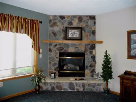 Cozy living room with a stone fireplace, mantle, window, plants, and furnishings.