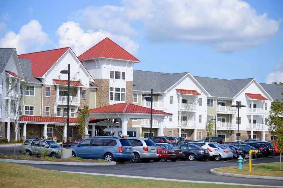 Exterior view of a multi-story senior living facility with red roofs and parked cars.
