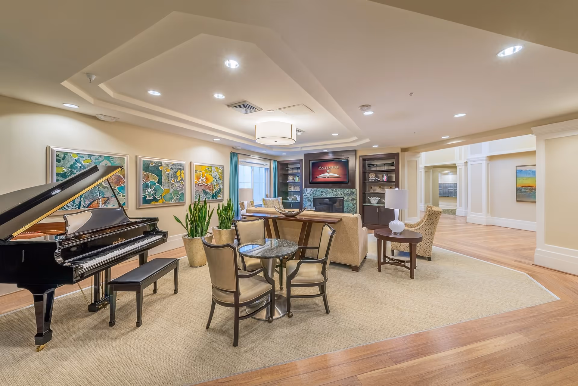 Bright communal lounge with a grand piano, seating and conversation area, TV over a fireplace, and wall artwork.