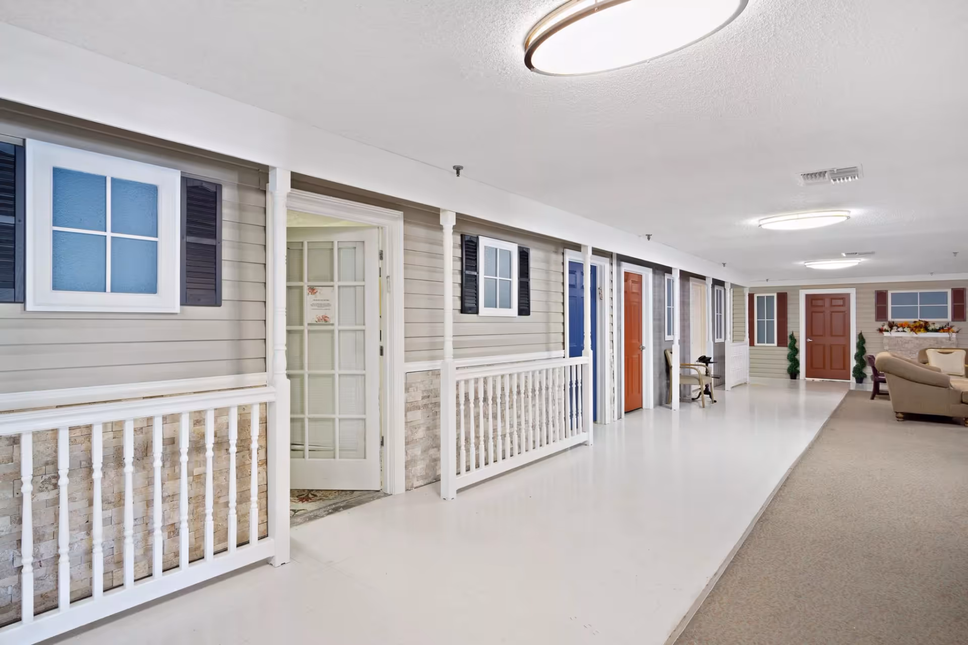 Indoor corridor resembling front porches with multiple apartment-style doors and a seating area.