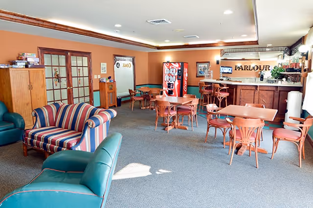 A spacious common room with sofas, multiple small tables and chairs, a vending machine, and a small bar area labeled 'PARLOUR'.