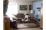 Small living room with a sofa, armchair, coffee table, and wall decorations lit by a window.