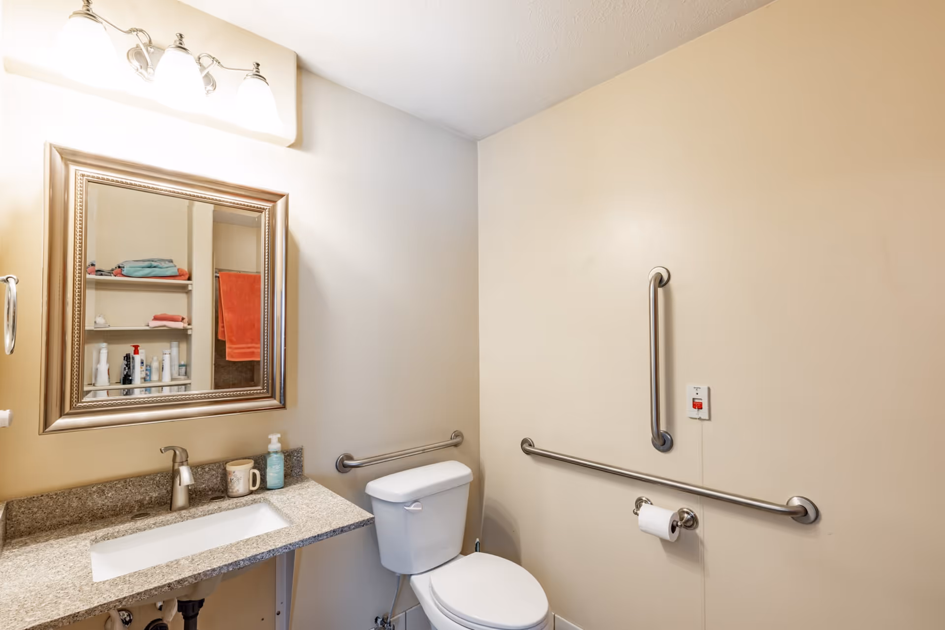 Accessible bathroom with a sink and mirror on the left and a toilet with horizontal and vertical grab bars on the right.