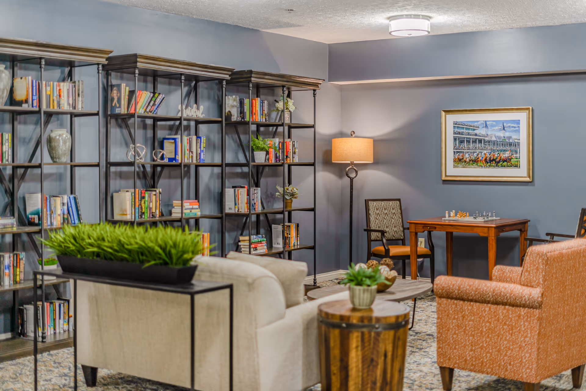 Communal lounge with bookshelves, sofas and chairs, a floor lamp, and a table with a chess set.