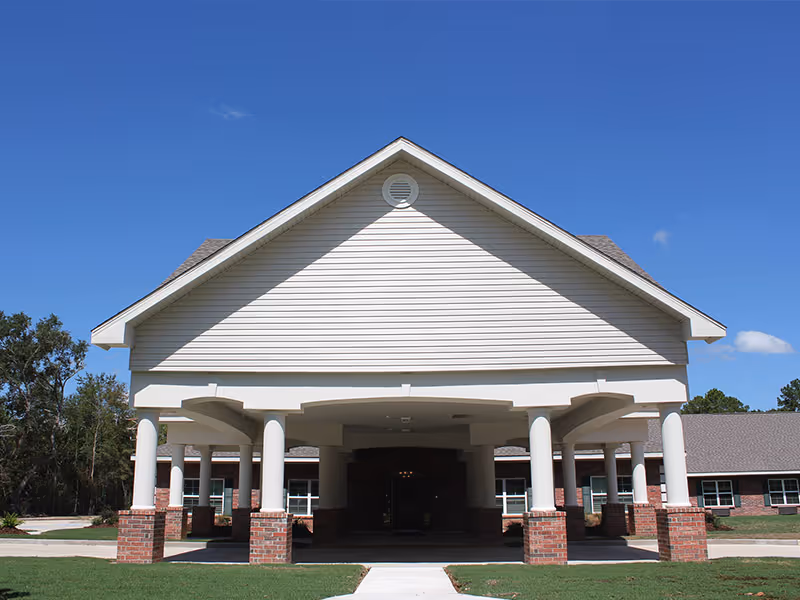 Front exterior view of Encore Healthcare & Rehabilitation building with a large covered entrance supported by white columns with brick bases, surrounded by green grass and trees under a clear blue sky.