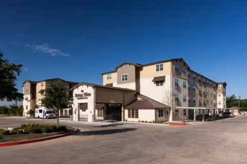 Exterior view of Heritage Village Residences building with entrance, parking, and clear blue sky.