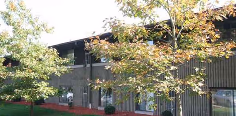Exterior view of a brown wood-paneled senior living building with trees in foreground.