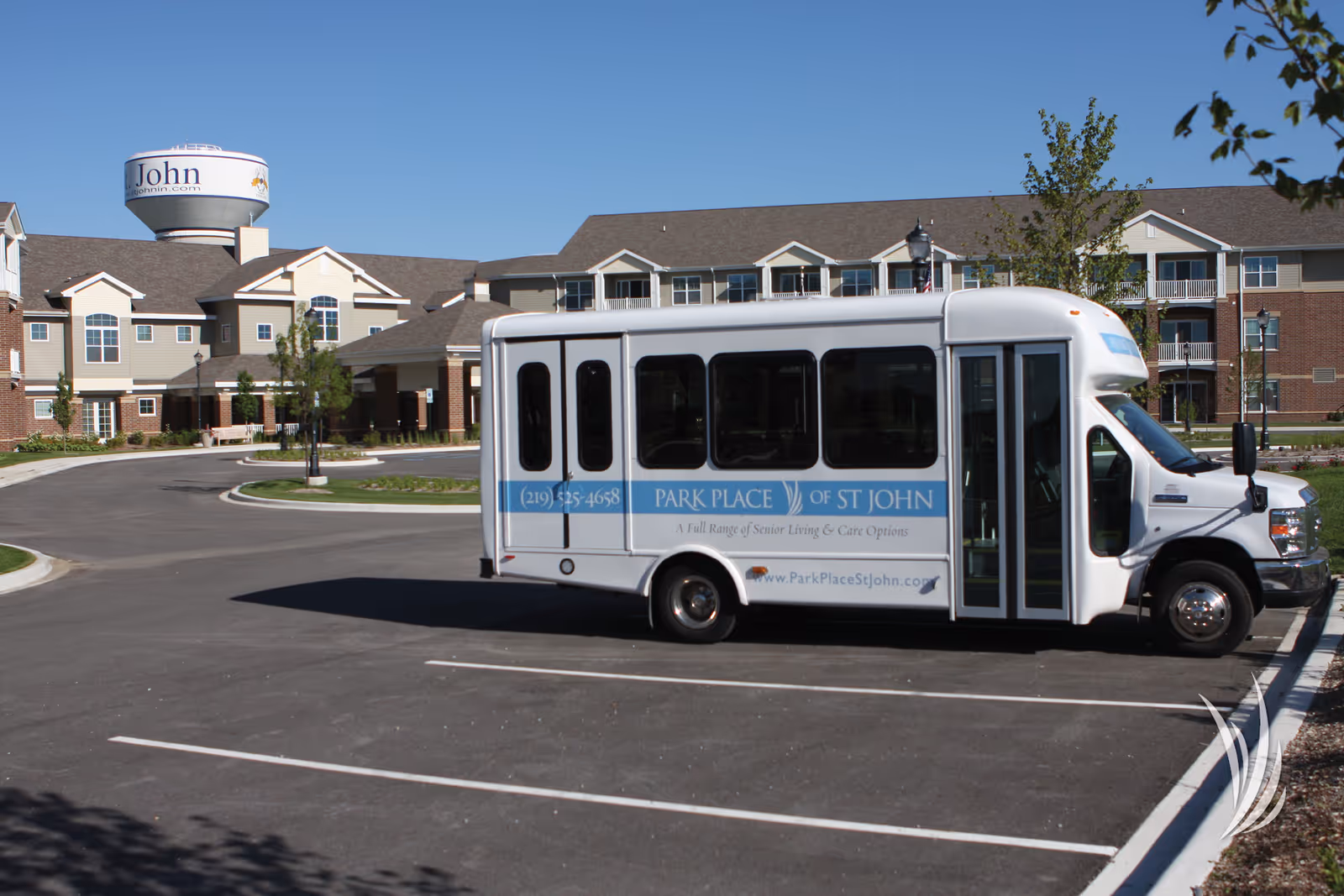A white Park Place of St John shuttle bus parked in front of a multi-story senior living building under a clear blue sky.
