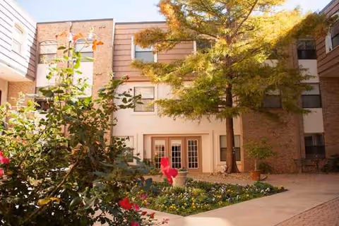 Exterior view of University Place Independent Living building with a courtyard, flowers, and trees.