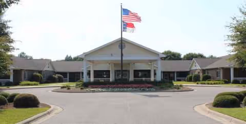 Front exterior of Glenflora senior living, circular driveway and flagpole with landscaping.
