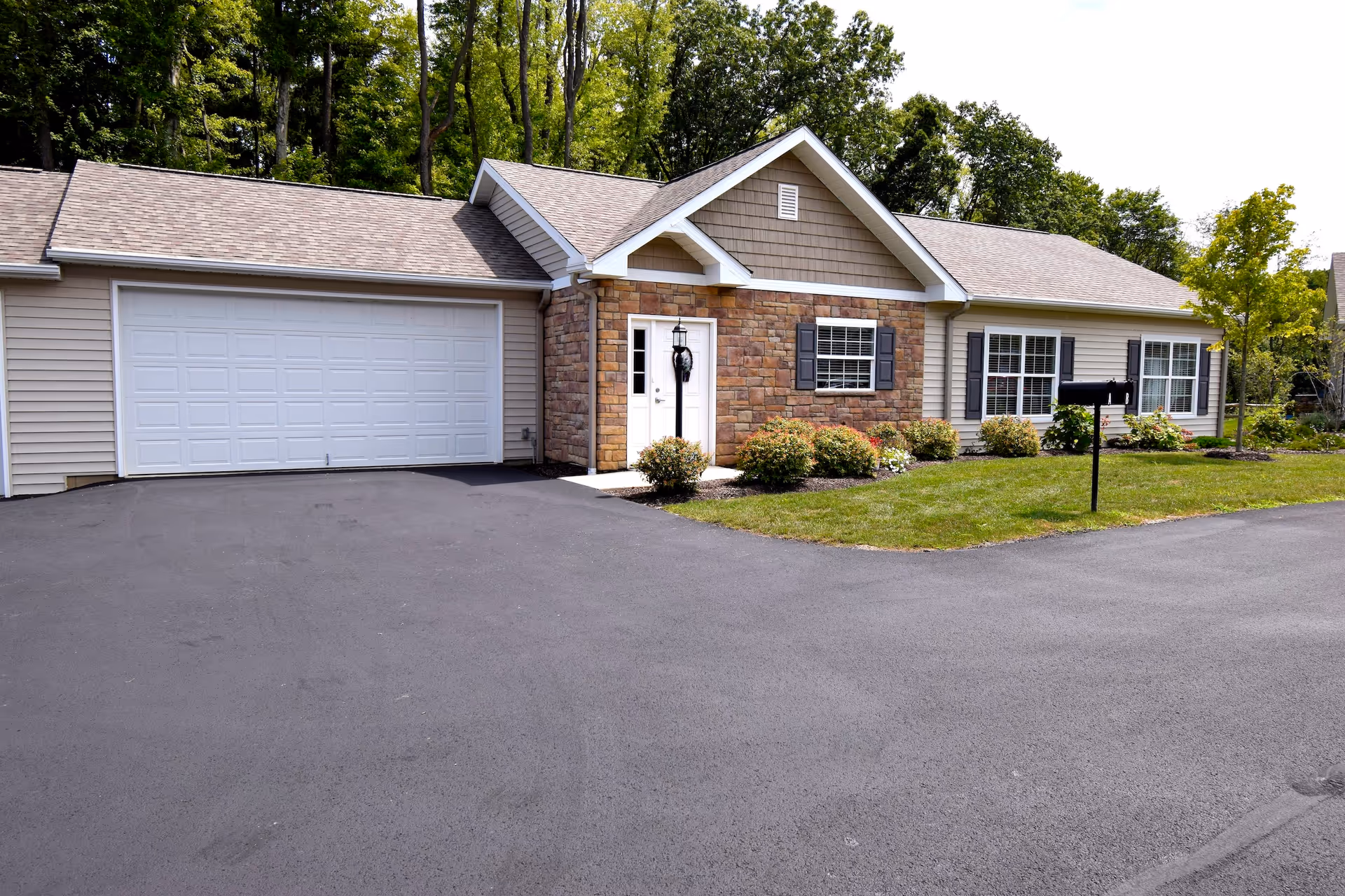 Single-story senior living facility with attached two-car garage, stone facade, and manicured front lawn.