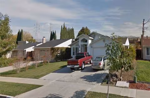 A suburban single-story house with a driveway, two parked cars, and a front yard.