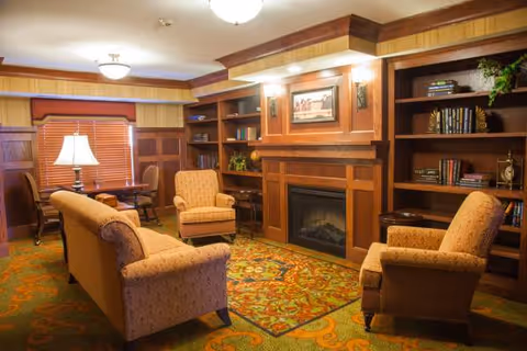 Cozy sitting room with upholstered sofas and armchairs arranged around a fireplace and built-in bookshelves.