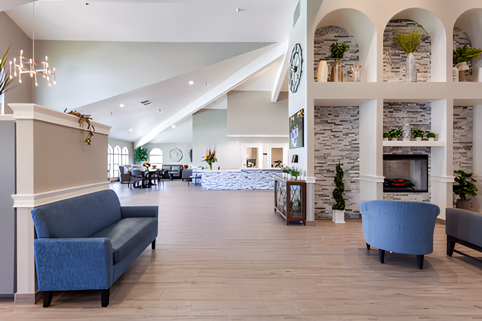 Spacious assisted living lobby with vaulted ceiling, seating areas, a fireplace, and a reception desk in the background.