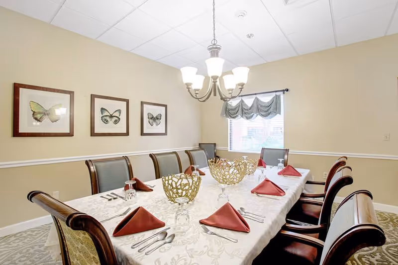 Formal dining room with a long table set with red napkins, decorative centerpieces, a chandelier, and butterfly artwork on the wall.