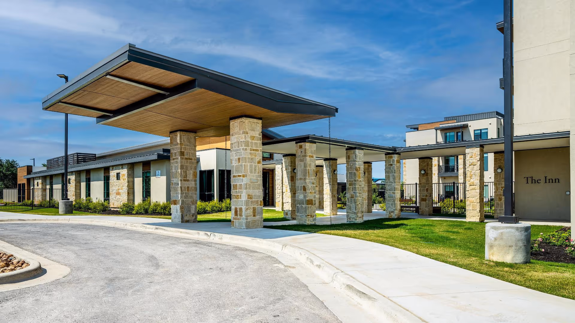 Covered porte-cochère with stone columns at the entrance of a modern senior living building labeled "The Inn".