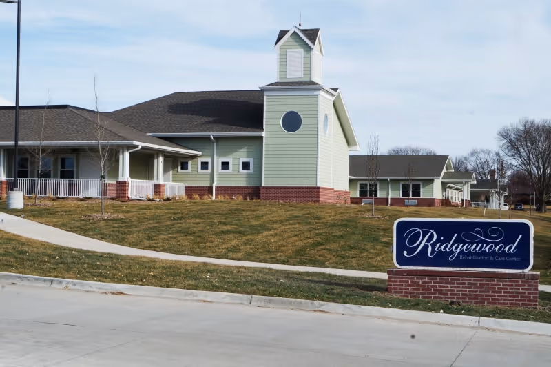 Front exterior of Ridgewood Rehab & Care Center with a lawn, walkway and a sign reading 'Ridgewood'.