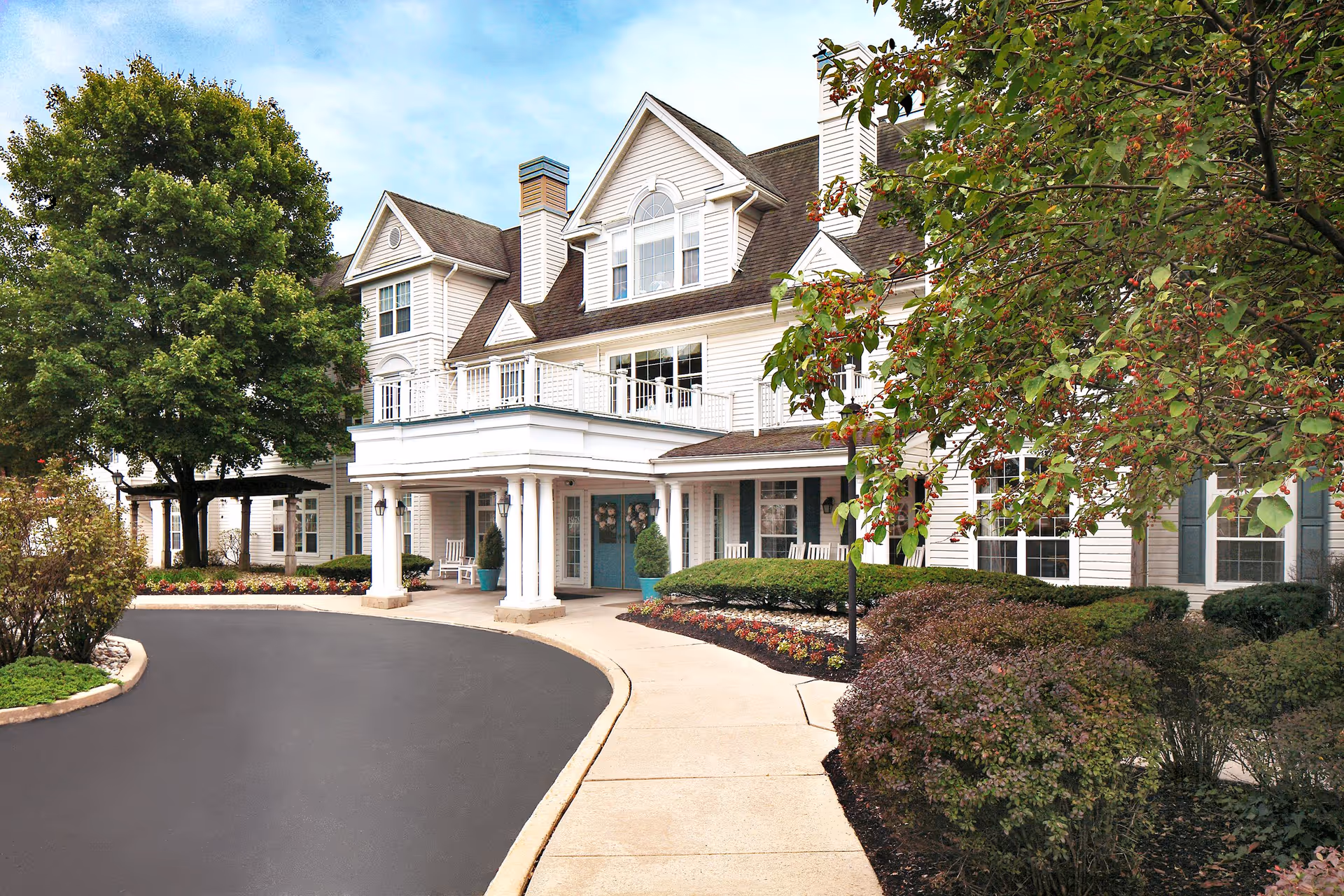 A large senior living facility exterior with a curved driveway and landscaped entrance.
