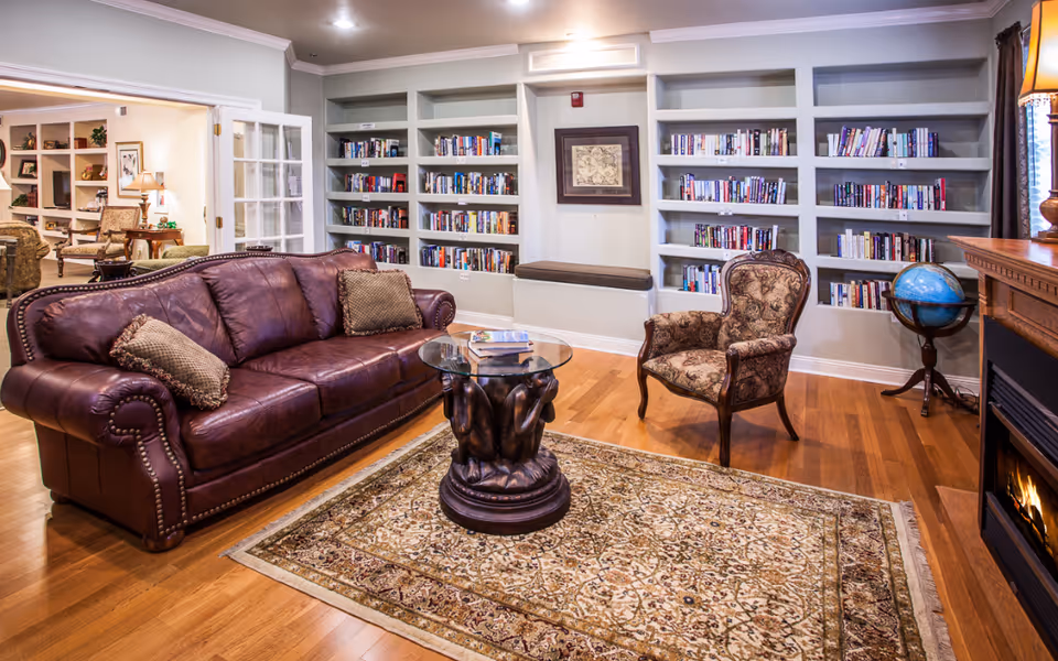 Cozy living room with a leather sofa, patterned armchair, glass-top coffee table, built-in bookshelves and a fireplace.