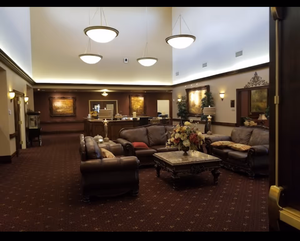 Spacious furnished lobby with leather sofas, a coffee table with a floral arrangement, framed artwork, and hanging pendant lights.