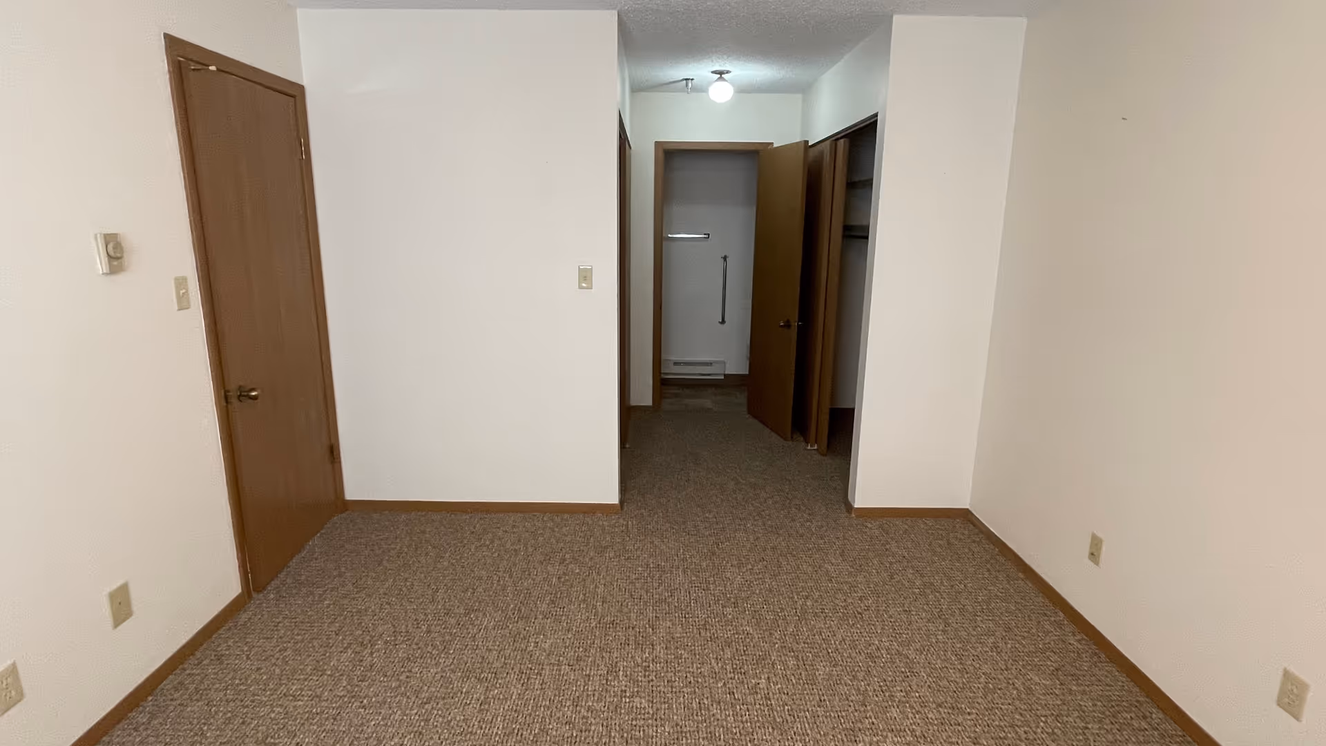 Narrow interior hallway in a senior living unit with carpet and open doors.