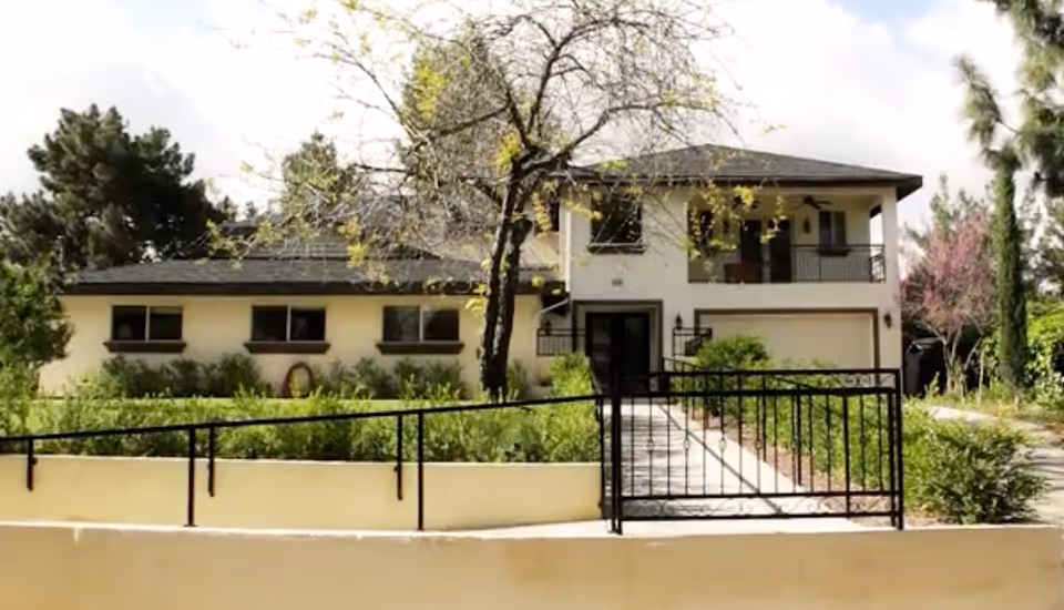 Two-story stucco building with a gated entrance, front walkway, balcony and landscaped yard.