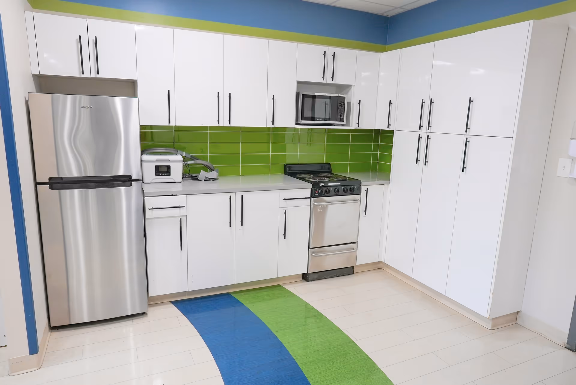 A modern kitchen with white cabinets and green backsplash in a senior living facility.