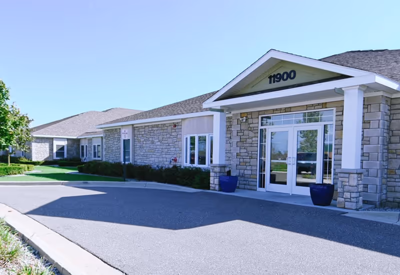 Exterior view of Vista Springs Washington Place entrance with stone facade, glass doors, and planters.