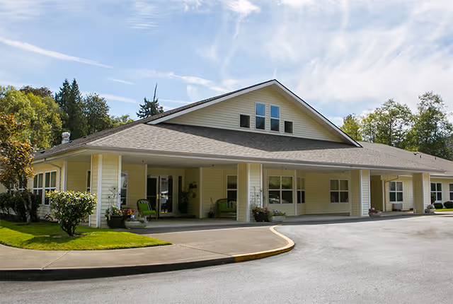 Front exterior of a single-story yellow building with a covered entrance, driveway, and landscaped lawn.