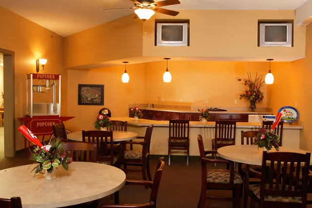 Community dining area with round tables and chairs, a popcorn machine, and a serving counter with pendant lights.