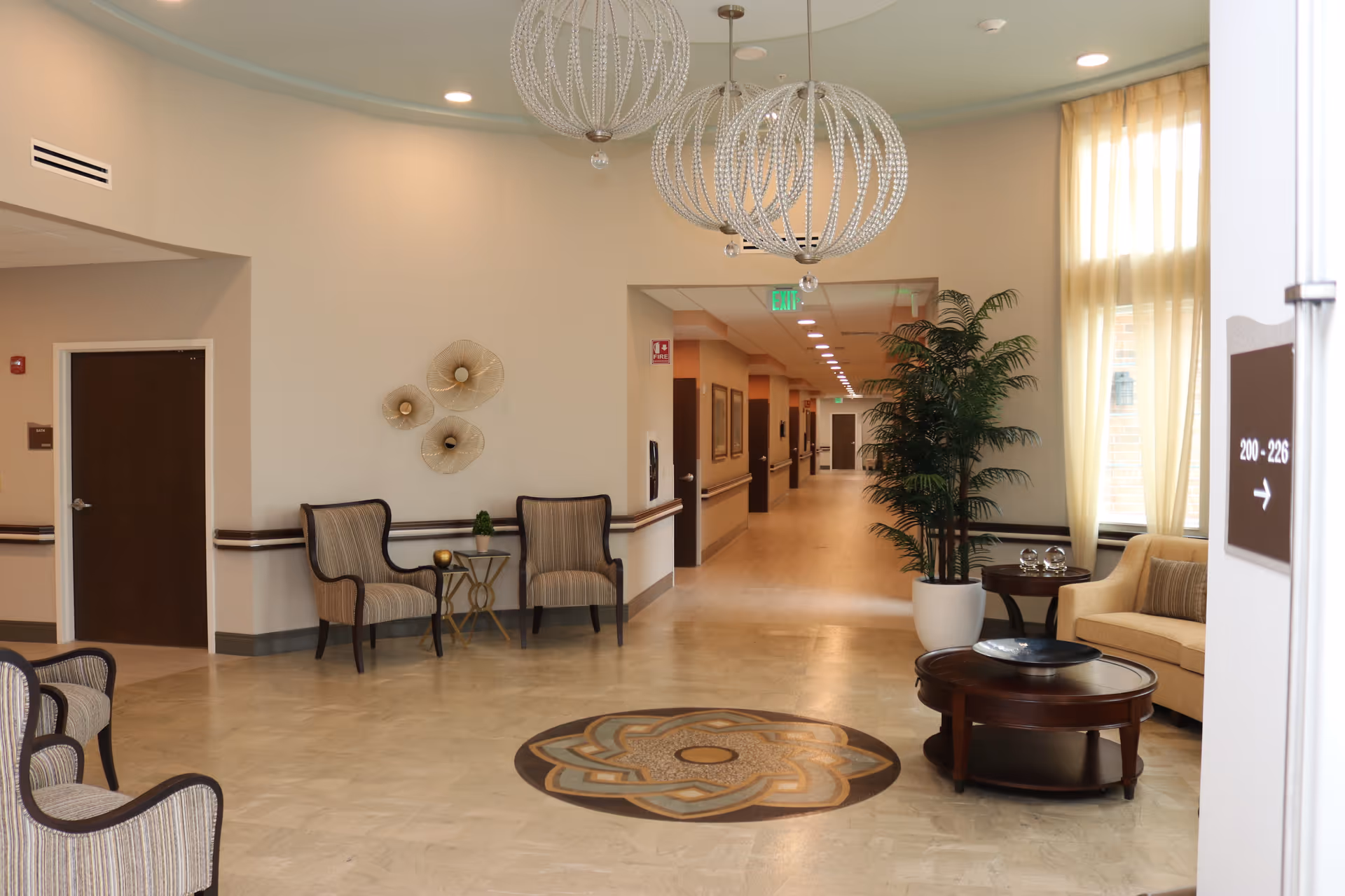 Lobby seating area in a senior living facility with chairs, tables, decorative lighting and a central hallway.