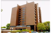 Tall brick senior care building with many windows and surrounding trees.