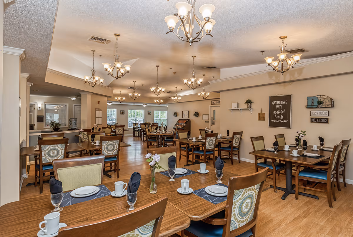 Dining room with multiple set wooden tables and chairs, chandeliers, and wall decor.